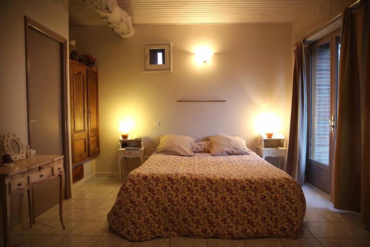 Un dormitorio con cama, mesitas de noche, cómoda, armario y una ventana pequeña.