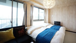 Una habitación de hotel moderna con una cama grande, un pequeño sofá y un ventanal con vistas a la ciudad.
