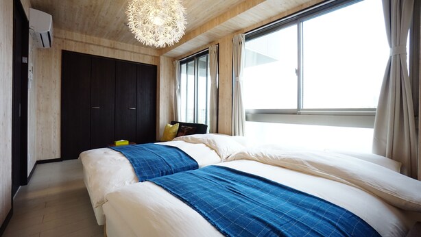 Un dormitorio con dos camas, techo de madera, un ventanal grande y una lámpara colgante.