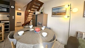 Un coin repas avec une table ronde, des chaises, un four à micro-ondes, un réfrigérateur, un escalier et un tableau accroché au mur.