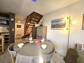 Un coin repas avec une table ronde, des chaises, un four à micro-ondes, un réfrigérateur, un escalier et un tableau accroché au mur.