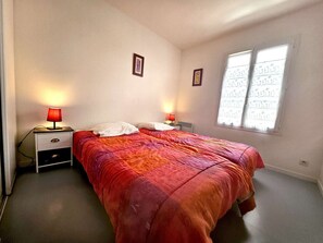 Een slaapkamer met een bed, twee nachtkastjes met lampen, een raam met gordijnen en een radiator.
