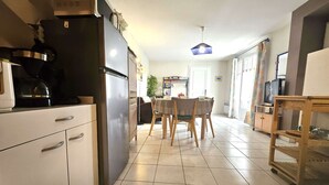 Une cuisine équipée d’un réfrigérateur, d’une cuisinière et de placards, un coin repas avec une table et des chaises, et un téléviseur en arrière-plan.