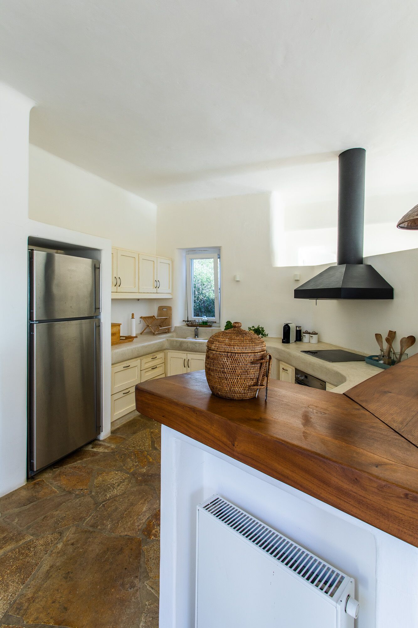 A modern kitchen with white cabinets, a stainless steel refrigerator, a large woven basket, and a black range hood.