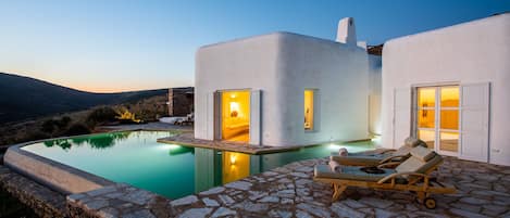 A modern villa with a swimming pool, stone flooring, and a view of the landscape.