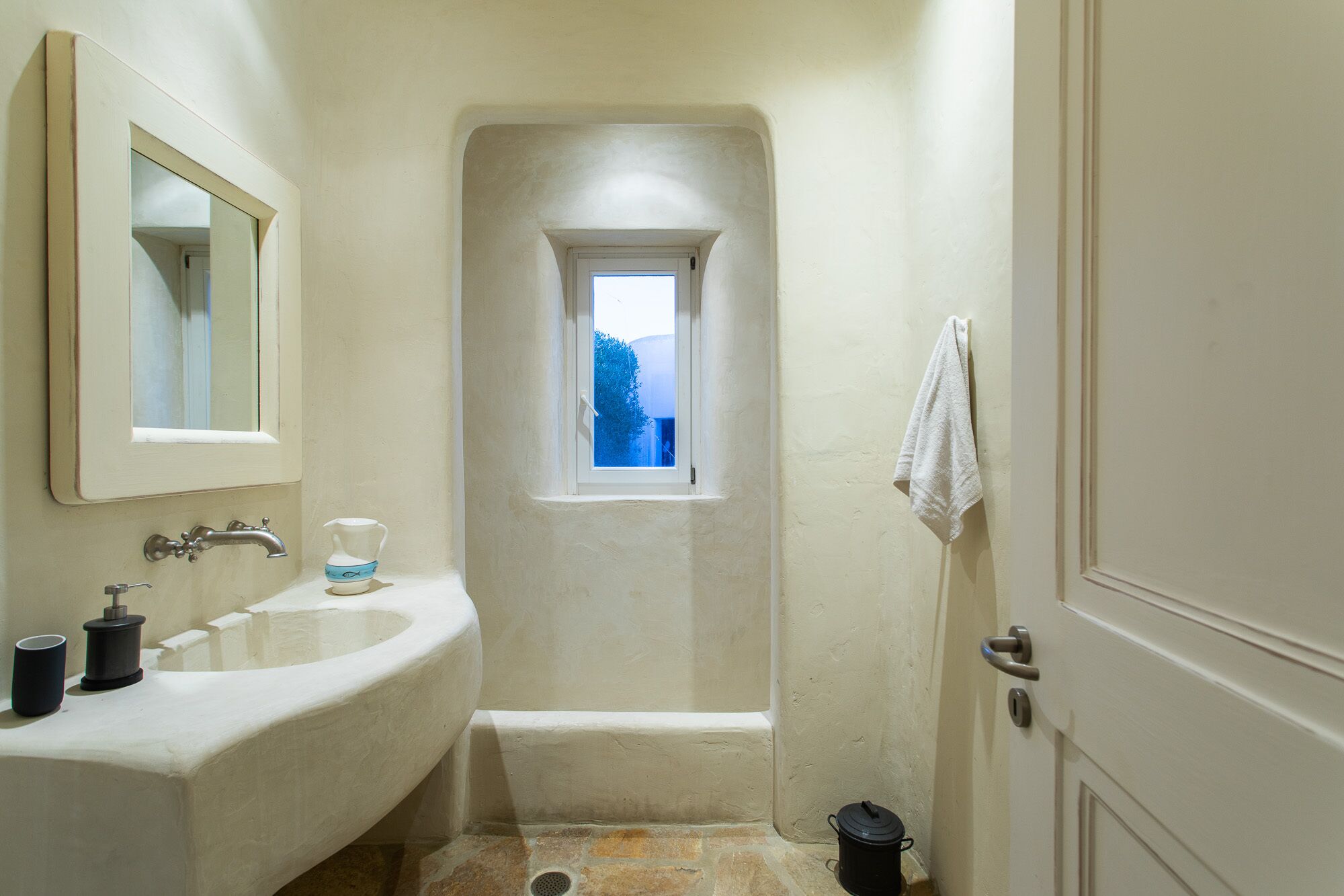 Un baño estrecho con ventana, lavabo y puerta.