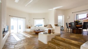 A spacious living area with a stone floor, a white sofa, a coffee table, and a dining area with chairs and a table. - Zen Residence in Lia beach (Mykonos)