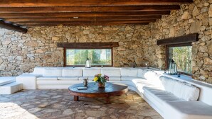 A stone-walled room with a wooden ceiling, a round coffee table, and a white sofa set. - Zen Residence in Lia beach (Mykonos)