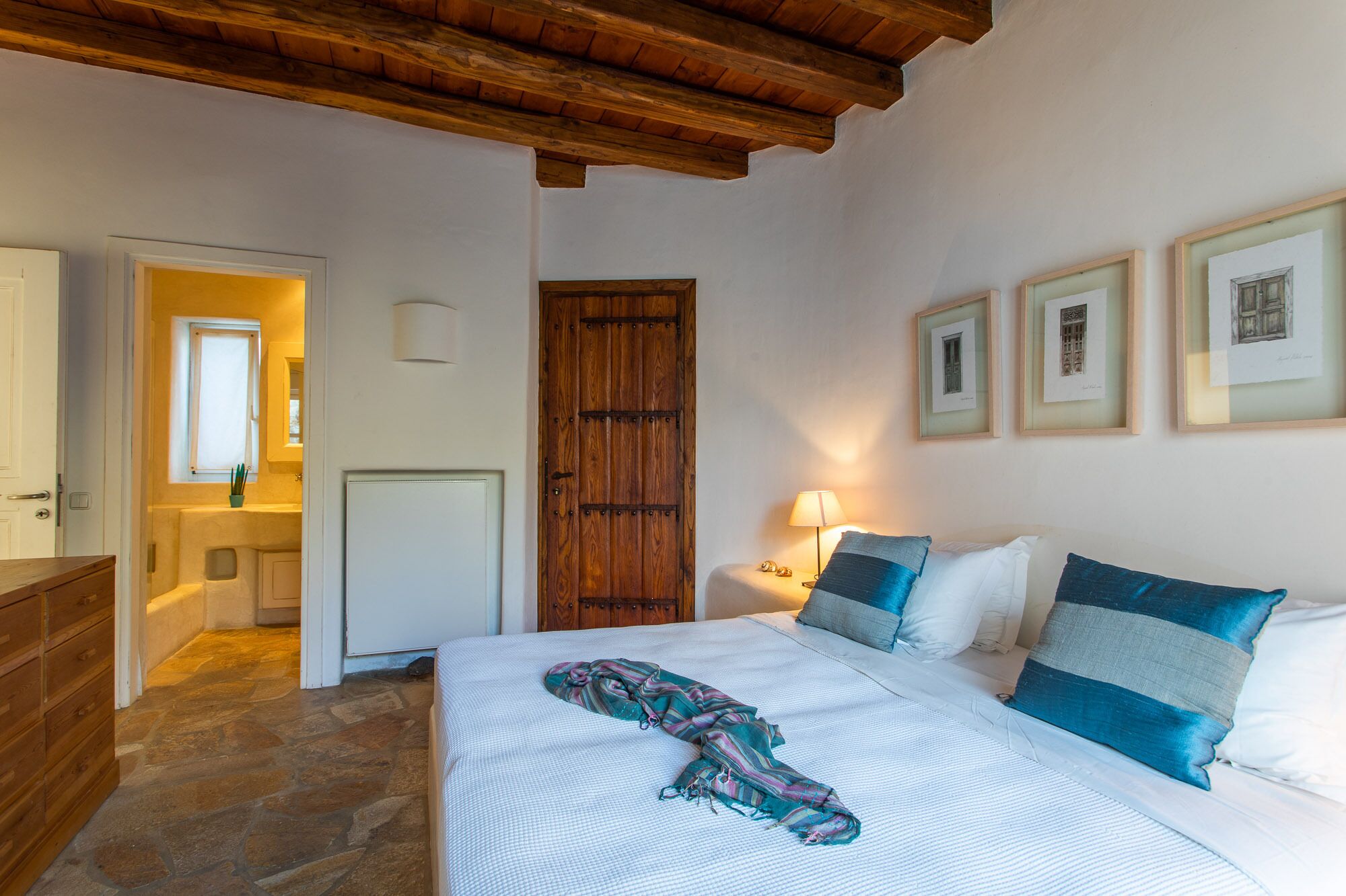 Une chambre à coucher avec un lit, une porte en bois, une table de chevet, une lampe et des tableaux encadrés accrochés au mur.