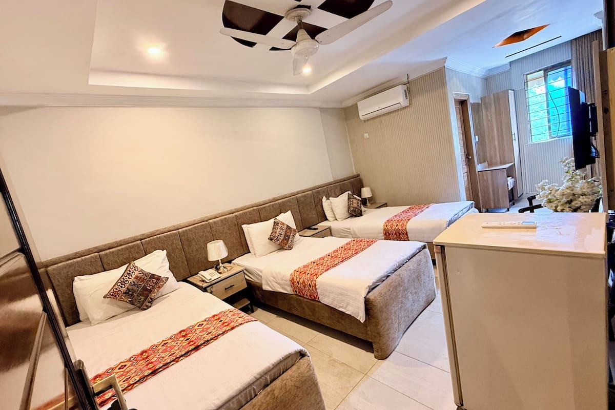 A hotel room with two beds, a desk, a chair, a TV, and an air conditioning unit.