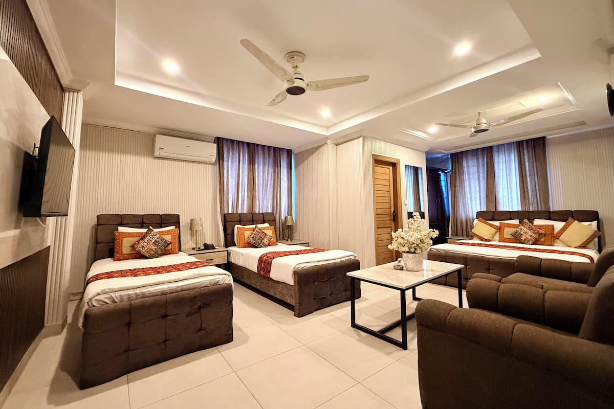 A hotel room with two beds, a sofa, a coffee table, and a ceiling fan.