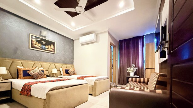 A hotel room with a large bed, a sofa, a ceiling fan, an air conditioning unit, and a painting on the wall. - Hotel Islamabad Premiere Inn (Islamabad)