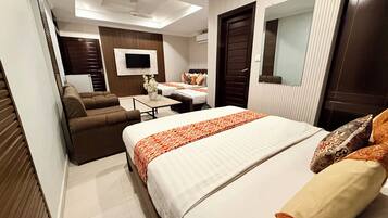 Habitación de hotel con una cama grande, un sofá, una mesita, un televisor y un espejo.