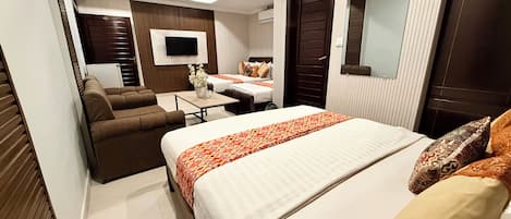 Habitación de hotel con una cama grande, un sofá, una mesita, un televisor y un espejo.