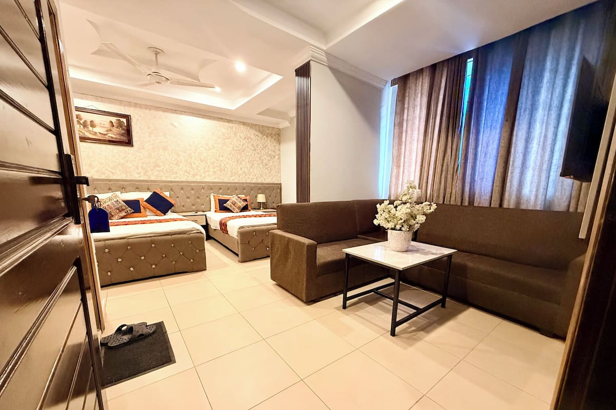 A hotel room with a bed, two sofas, a small table with a vase, and a ceiling fan.