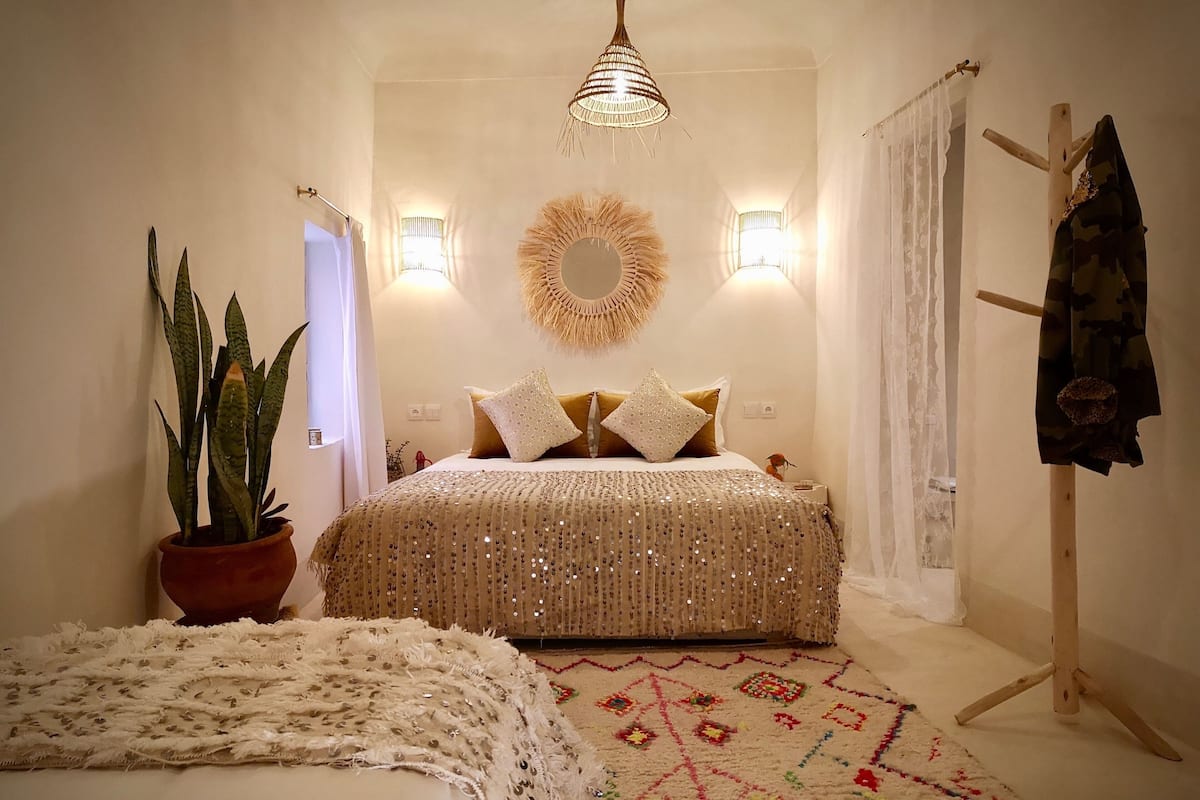 A bedroom with a bed, a hanging light fixture, a mirror, and a potted plant.