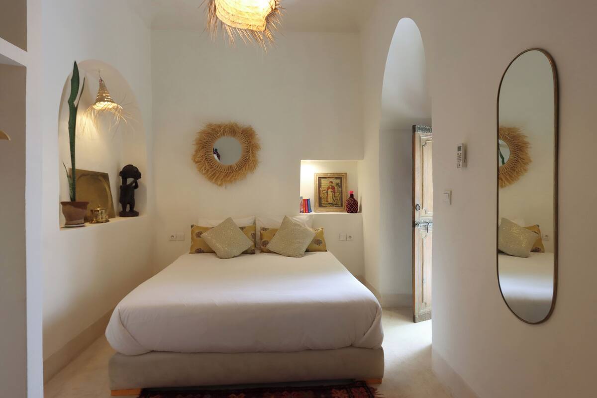 A bedroom with a large bed, a mirror, and a wall-mounted wreath.
