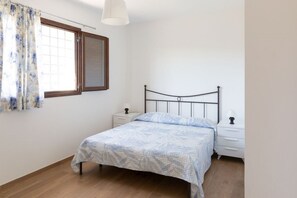 A bedroom with a bed, two bedside tables, a window with curtains, and a hanging light fixture.