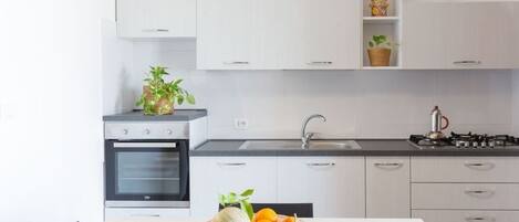 A modern kitchen with white cabinets, a gas stove, an oven, and a bowl of fruit on the counter.