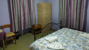 A bedroom with a bed, a wooden wardrobe, a chair, a small table, and a trash bin. - Pinguino Hostel Athens (Athens)