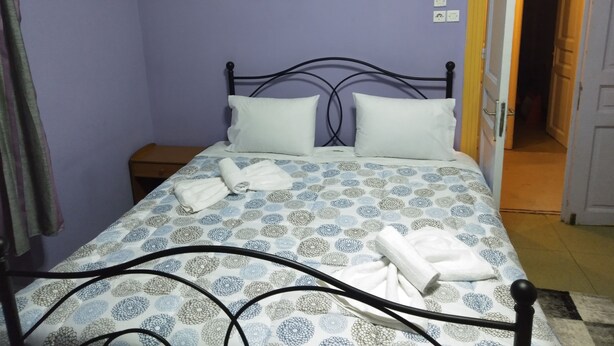 A bedroom with a bed, pillows, a bedside table, a wall-mounted picture, and an open door leading to another room. - Pinguino Hostel Athens (Athens)