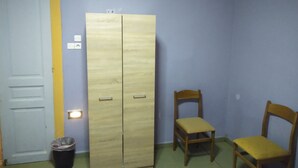 A room with a wardrobe, two chairs, a trash bin, and a door. - Pinguino Hostel Athens (Athens)