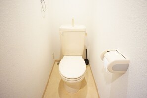 De petites toilettes blanches, dotées d’une poignée de chasse d’eau et d’un porte-rouleau de papier toilette fixé au mur.