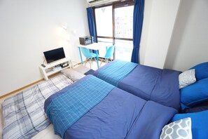Une chambre avec deux lits, un bureau avec un ordinateur, une chaise et une fenêtre avec des rideaux.