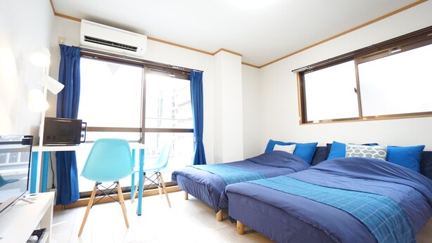A bedroom with two beds, a desk, a chair, and an air conditioning unit. - Terry's Apartment Shinsaibashi I M04B (Osaka)