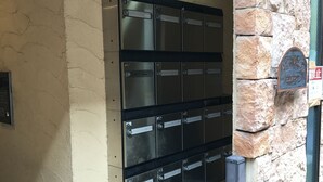 A row of metal mailboxes with numbered slots, mounted on a beige wall with a stone accent. - Terry's Apartment Shinsaibashi I M04B (Osaka)