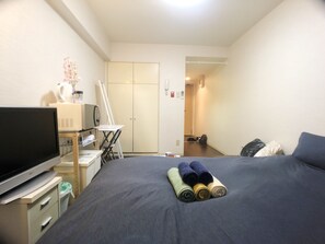 Et hotelværelse med seng, skrivebord med computer, stol, garderobeskab og fjernsyn.
