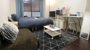 A compact hotel room with a bed, a sofa, a small table, and a desk with a computer and microwave. - Smart Stay Tokyo L333 (Tokyo)