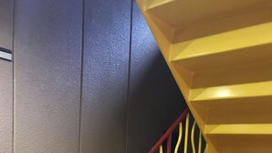 Eine Treppe mit gelben und roten Geländern, Holzbodenstufen und einem Feuerlöscher auf der rechten Seite.