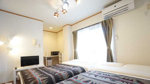 Ein Hotelzimmer mit zwei Betten, einem Fernseher, einem Schreibtisch und einer Klimaanlage.