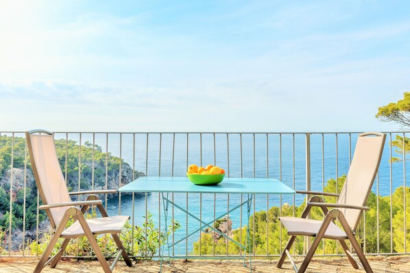 A balcony with two chairs and a table, overlooking a scenic coastal view.