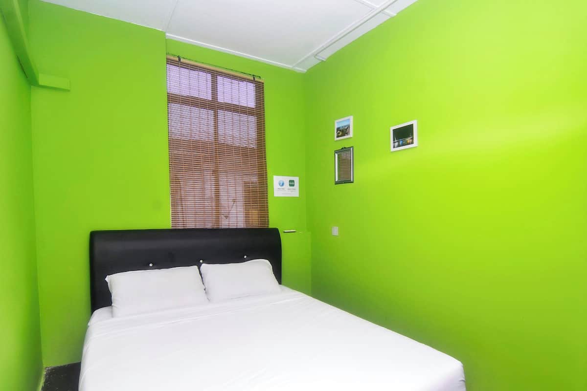 A room with a bed, a window with blinds, and a small sign on the wall.