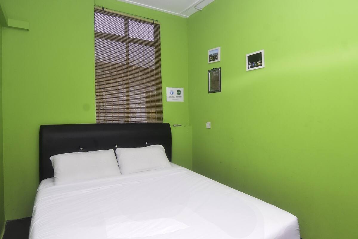 A room with a bed, green walls, a window with blinds, and a small picture on the wall.