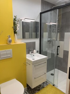 Un baño con un lavamanos blanco, un espejo, una cabina de ducha de vidrio y una pared de acento amarilla.