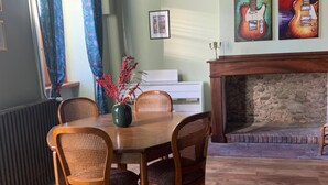 A dining area with a wooden table and chairs, a fireplace, and guitar-themed artwork on the wall. - La Maison d'Amalaurille (Estancarbon)