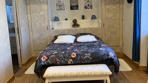 A bedroom with a large bed, a bench, and a small table. There are three wall-mounted shelves with decorative items. - La Maison d'Amalaurille (Estancarbon)