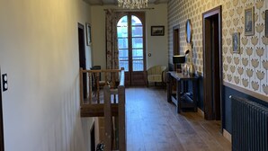 A spacious hallway with wooden flooring, a chandelier, and a view of a room with a window and a door. - La Maison d'Amalaurille (Estancarbon)