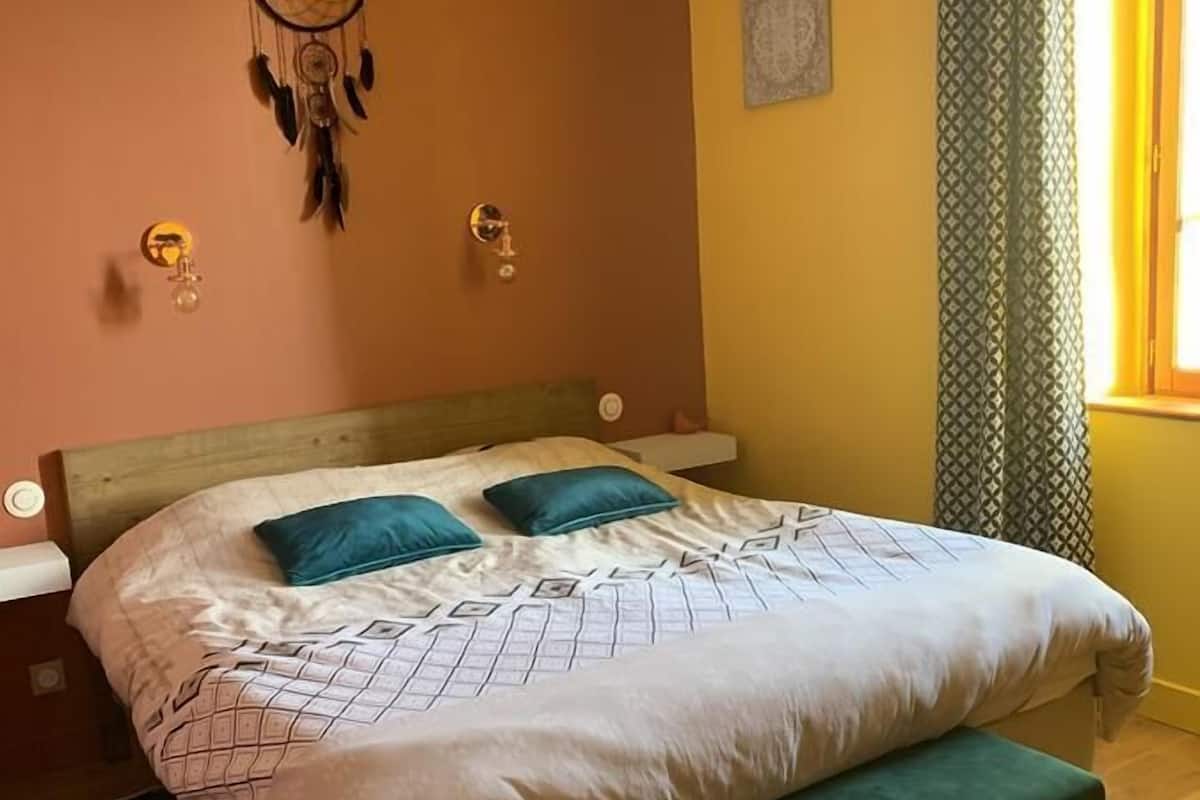 A bedroom with a bed, a dreamcatcher, a green bench, and a window with curtains.