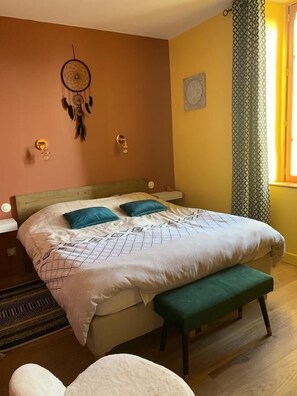 Un dormitorio con cama, un atrapasueños, un banco verde y una ventana con cortinas.