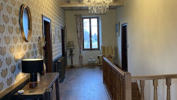 A spacious hallway with wooden flooring, a chandelier, and a staircase with wooden railings.