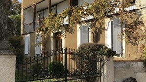A two-story building with a balcony, a wrought iron fence, and a small garden area. - La Maison d'Amalaurille (Estancarbon)