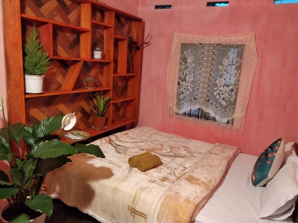 Un dormitorio con cama, una estantería de madera con plantas en macetas y un tapiz decorativo en la pared.