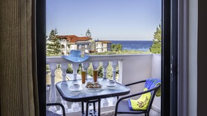 Ein Balkon mit Tisch für zwei Personen, einem Stuhl und Blick auf das Meer sowie Gebäude im Hintergrund.
