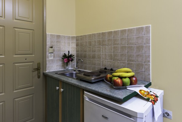 Una cocina con un lavamanos, una encimera y un escurreplatos. Hay plátanos, manzanas y un florero con flores sobre la encimera.
