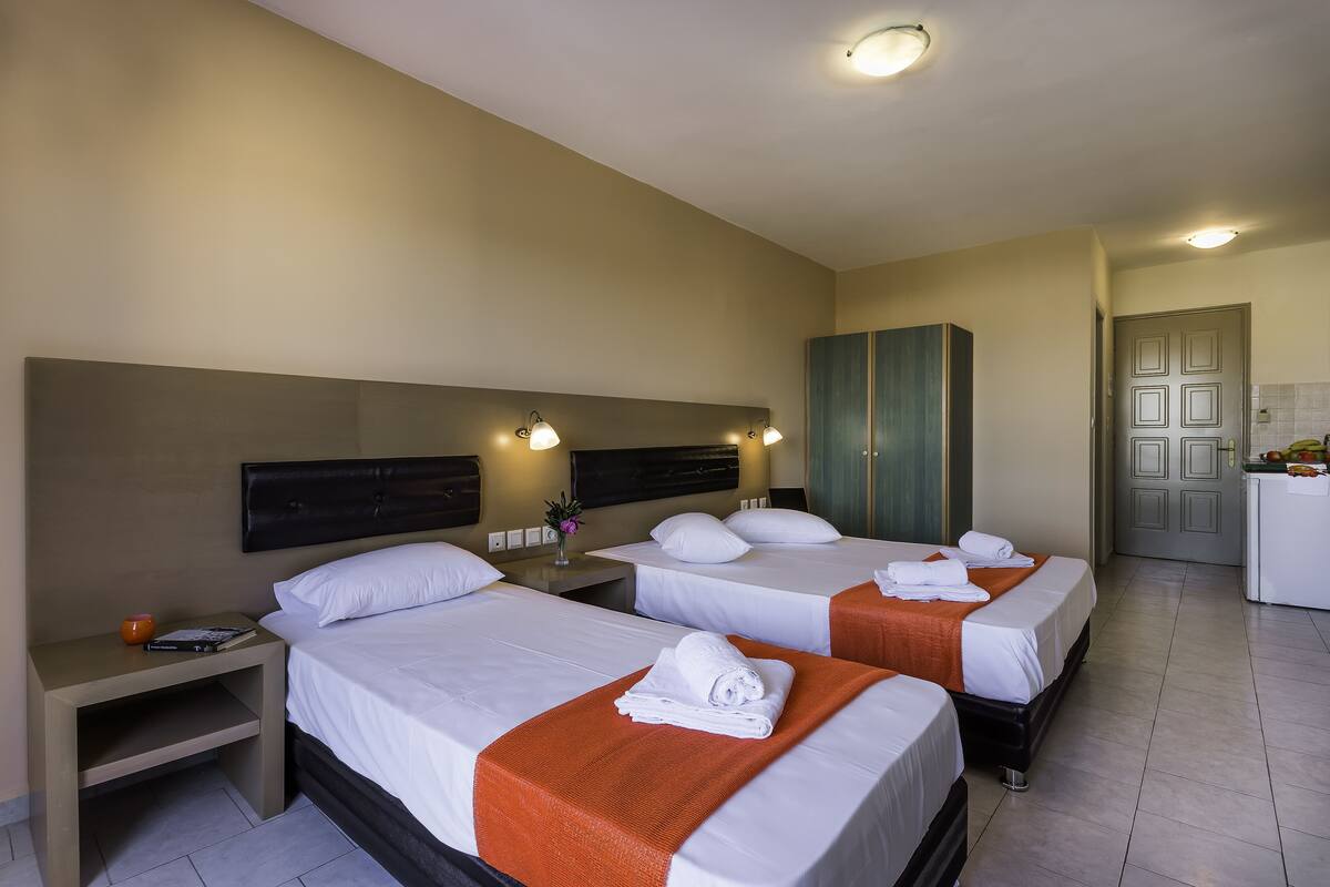 A hotel room with three beds, a nightstand, a desk, and a bathroom visible through an open door.