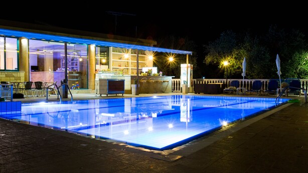 Ein Poolbereich bei Nacht mit Bar und Sitzgelegenheiten neben einem Gebäude mit großen Fenstern.